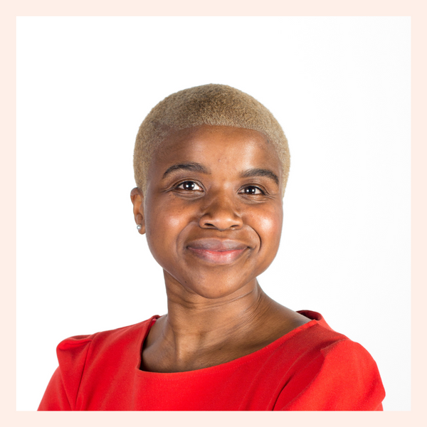 Gaelle Buruel woman of colour with short cropped blonde hair, brown skin smiling with her lips shut at the camera. She is wearing a bright red top with a round neck.