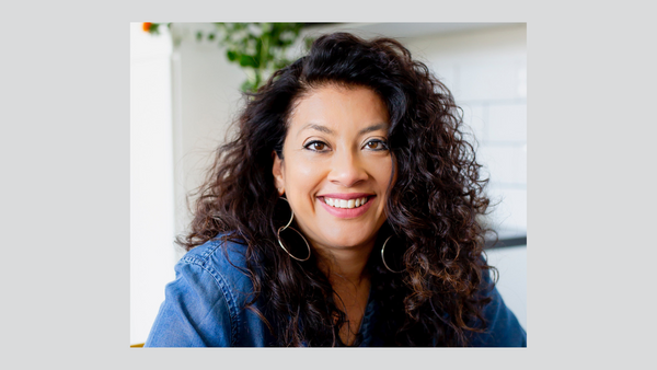 mallika-basu-food -and-drink-industry-commentator-and-communications-and-strategy-consultant-head-shoulders-shot-facing-olive-skinned-woman-facing-camera-smiling-with-teeth-showing-dark-curly-side-parted-hair-denim-top
