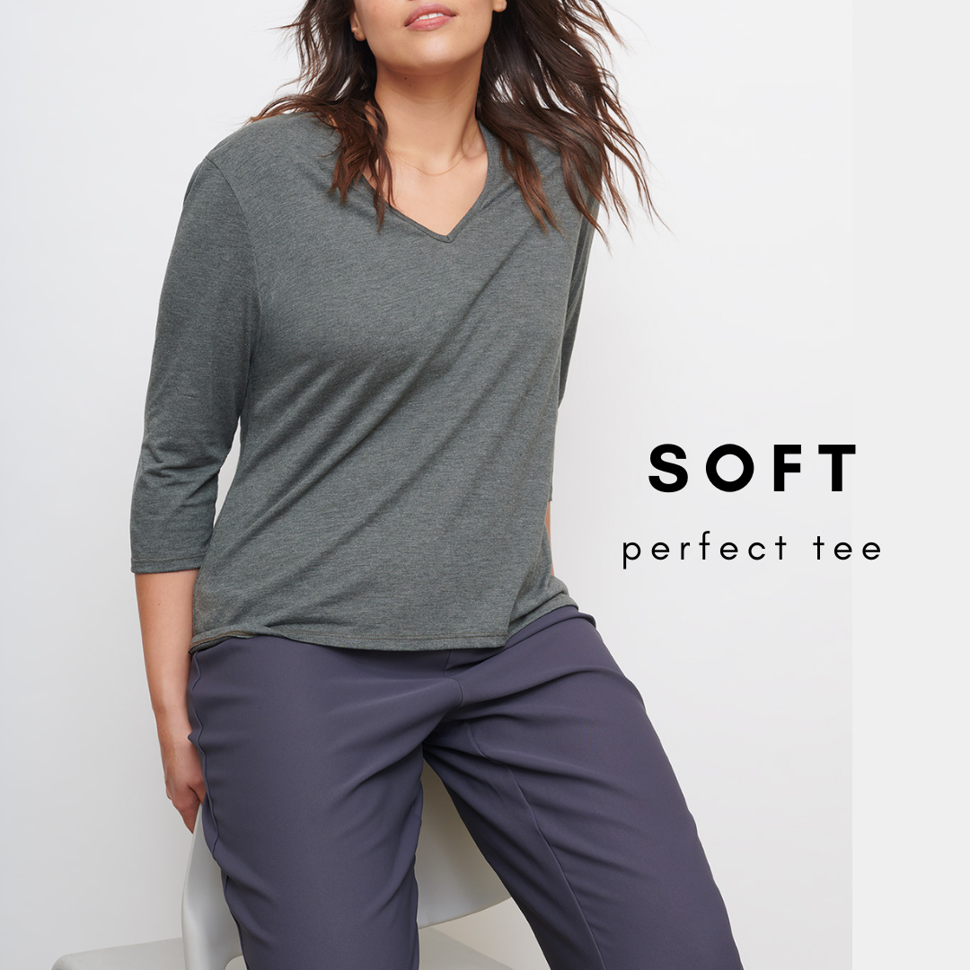 image of headless female model leaning on a white chair wearing a green v neck tee and grey trousers. 