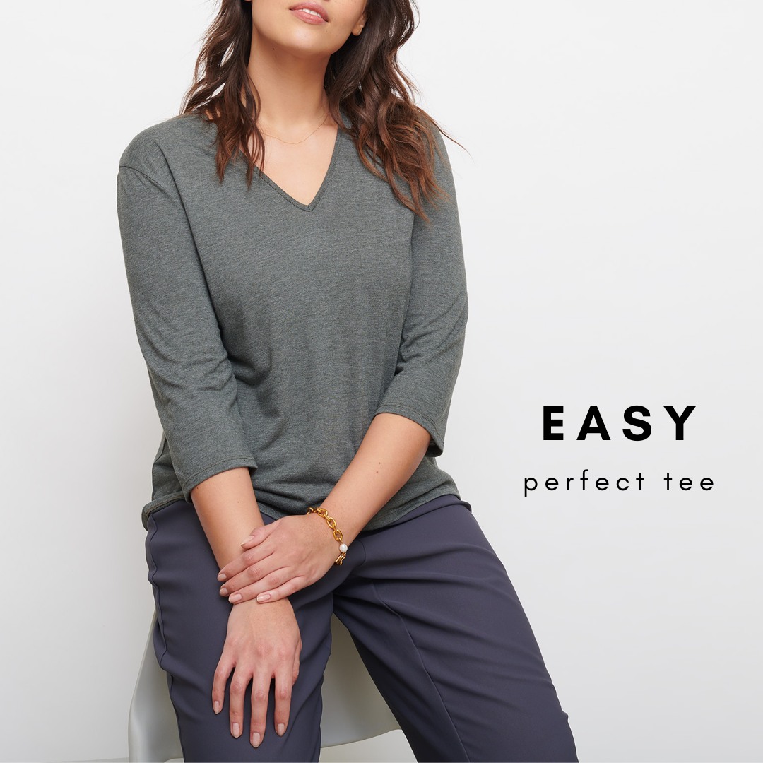 image of headless model leaning on a white chair wearing a green v neck tee and grey trousers.
